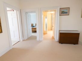 A hallway with beige carpet with three doorways leading to other rooms and a wooden cabinet on the side at Flat 3 Trearddur Bay