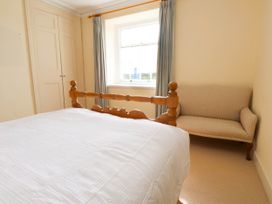 A bedroom with a wooden bed a beige sofa a window with curtains and built in wardrobes at Flat 3 in Trearddur Bay
