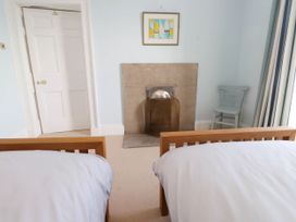 A bedroom with two single beds a fireplace a chair and a door at Flat 3 Trearddur Bay