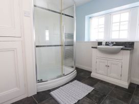 A bathroom with a shower enclosure a sink with cabinet a window and a floor mat at Flat 3 in Trearddur Bay