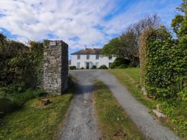 A gravel driveway leading to a white two-story house with stone pillars and greenery on the sides at Flat 3 in Trearddur Bay