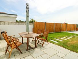 A patio with a wooden table and four wooden chairs next to a grass lawn and wooden fence at Ty Bach in Llanfaelog near Rhosneigr