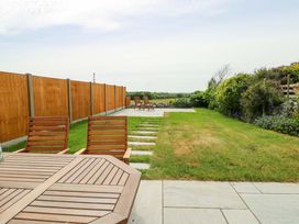 A garden with a wooden table and chairs a lawn a stone path wooden fence and shrubs at Ty Bach in Llanfaelog near Rhosneigr
