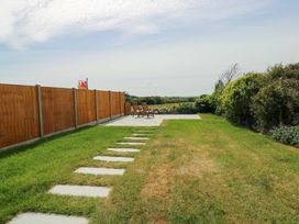 A garden with a wooden fence two chairs on a patio and a lawn with stepping stones at Ty Bach in Llanfaelog near Rhosneigr