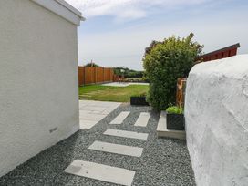 An outdoor pathway with stone slabs and gravel leading to a lawn area with wooden chairs and a wooden fence at Ty Bach in Llanfaelog near Rhosneigr