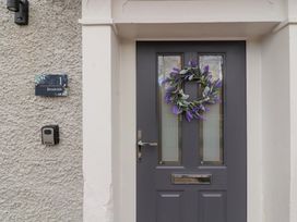A front door with two small windows and a wreath with purple flowers next to a wall plaque reading 1 Brookside in Warcop