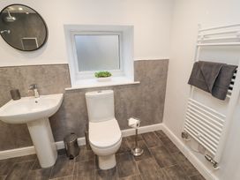 A bathroom with a pedestal sink and round mirror a toilet and freestanding toilet paper holder a towel rack with towels and a frosted window with a plant on the sill at 1 Brookside in Warcop