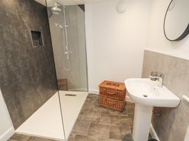A bathroom with a walk-in shower a pedestal sink a round mirror and two wicker baskets on the floor at 1 Brookside Warcop