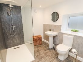 A bathroom with a shower area a toilet a sink a round mirror a window and a wicker basket at 1 Brookside Warcop