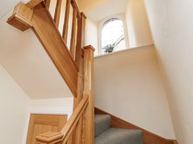 A staircase with wooden banisters and grey carpet under a window with a potted plant at 1 Brookside in Warcop