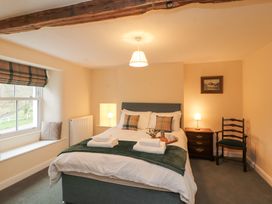 A bedroom with a bed with pillows and folded towels a window seat with cushions a wooden nightstand with a lamp and a chair at 1 Brookside in Warcop