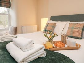 A bedroom with a bed with plaid pillows towels and a breakfast tray with croissant and juice at 1 Brookside in Warcop