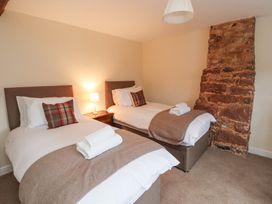 A bedroom with two single beds a bedside table with lamp and exposed brick wall at 1 Brookside in Warcop