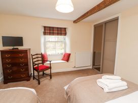 A bedroom with two beds a wooden chest of drawers with a television a wooden chair and a window with red cushions at 1 Brookside in Warcop