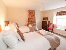 A bedroom with two beds a wooden chest of drawers a chair and a window seat at 1 Brookside in Warcop