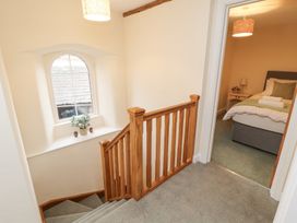A hallway with wooden staircase railing a window with flowers on the sill and a bedroom with a bed and bedside table at 1 Brookside in Warcop