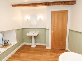 A bathroom with a pedestal sink a wooden door and a window with a plant on the sill at 1 Brookside Warcop