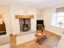 A living room with a fireplace a wooden coffee table a television and a window with flowers at 1 Brookside in Warcop
