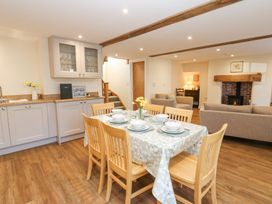 A dining area with a table set for six next to a kitchen with cabinets and a living room with sofas and a fireplace at 1 Brookside in Warcop