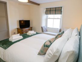 A bedroom with a bed with white linens and green plaid pillows a wooden chest with a television and a window seat with cushions at 1 Brookside in Warcop