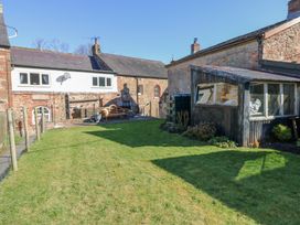 A grassy backyard with a bench and a shed beside stone buildings at 1 Brookside in Warcop