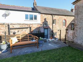 A wooden bench with a cushion and bottle on a concrete patio next to stone buildings at 1 Brookside in Warcop