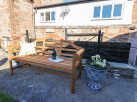 An outdoor seating area with a wooden bench a cushion a bottle of prosecco and two glasses next to two flower pots at 1 Brookside in Warcop
