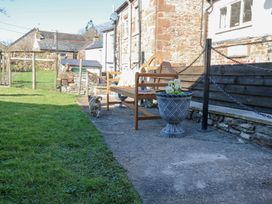 A wooden bench with cushions and flowerpots next to a stone building and a small dog on a paved path at 1 Brookside in Warcop