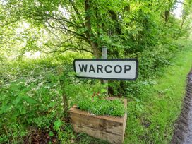 A road sign with warcop written on it surrounded by green plants and trees near a grassy path at 1 Brookside in Warcop