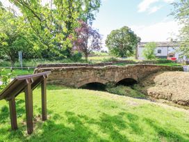 A stone bridge over a small stream with a wooden information board and trees at 1 Brookside in Warcop
