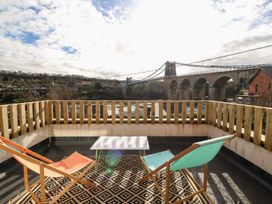 A balcony with two lounge chairs and a table overlooking a bridge and river at Ty Chwarel in Menai Bridge