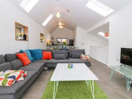A living room with a gray sectional sofa and colorful cushions near a white coffee table on a green rug at Ty Chwarel in Menai Bridge