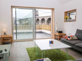 A living room with sliding glass doors overlooking a bridge a gray sofa with a blanket a white coffee table on a green rug and wooden side tables at Ty Chwarel in Menai Bridge