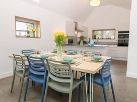 A dining table set with plates bowls glasses and cutlery surrounded by chairs in an open kitchen and dining area at Ty Chwarel in Menai Bridge