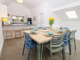 A dining area with a table set for eight and an open kitchen with stools at Ty Chwarel in Menai Bridge