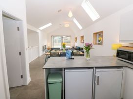 A kitchen area with a countertop and two small refrigerators next to a dining table with flowers in vases and a living area in the background at Ty Chwarel in Menai Bridge