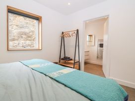 A bedroom with a bed covered in a blue quilt next to a window and an open door leading to a bathroom at Ty Chwarel in Menai Bridge