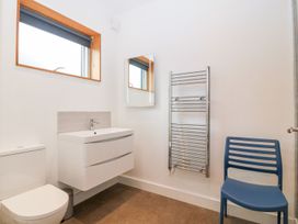 A bathroom with a toilet sink vanity mirror heated towel rail and blue chair at Ty Chwarel in Menai Bridge