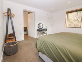 A bedroom with a bed covered in green bedding a window a chair a small desk with a mirror an open door a clothes rack and a laundry basket at Ty Chwarel in Menai Bridge