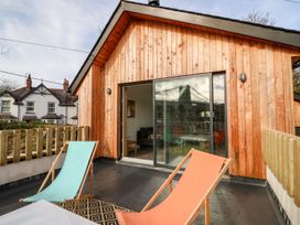 A balcony with two colored deck chairs facing a wooden cabin with sliding glass doors at Ty Chwarel in Menai Bridge
