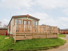 A wooden cabin with a fenced deck on a grassy area at 6 Sherwood in Carnforth near Tewitfield