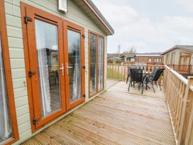 A wooden deck with a glass door and outdoor table and chairs at 6 Sherwood in Carnforth near Tewitfield