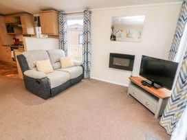 A living room with a sofa a television on a stand and a wall-mounted electric fireplace at 6 Sherwood in Carnforth near Tewitfield