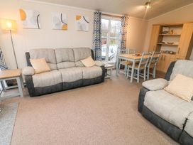 A living room with sofas a dining table chairs a floor lamp and a wooden cabinet at 6 Sherwood in Carnforth near Tewitfield