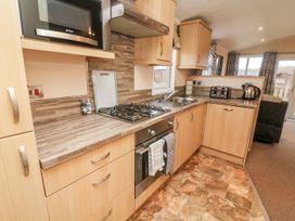 A kitchen with wooden cabinets a gas stove oven microwave kettle toaster and a sink at 6 Sherwood in Carnforth near Tewitfield