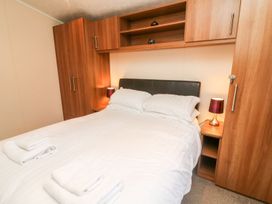 A bedroom with a double bed white bedding wooden built in wardrobes and bedside tables with lamps at 6 Sherwood Carnforth near Tewitfield