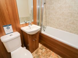 A bathroom with a toilet a sink with a mirror and a bathtub with shower at 6 Sherwood Carnforth near Tewitfield
