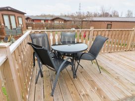 A wooden deck with a round glass table and four black mesh chairs at 6 Sherwood in Carnforth near Tewitfield