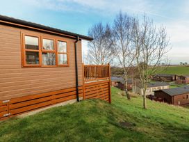 An exterior view of a wooden cabin on a grassy slope with trees and other cabins in the background at Finnbars Lodge in Richmond