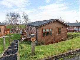 A brown wooden lodge with a black roof and a wooden deck on a grassy hill with a path leading to it at Finnbars Lodge in Richmond